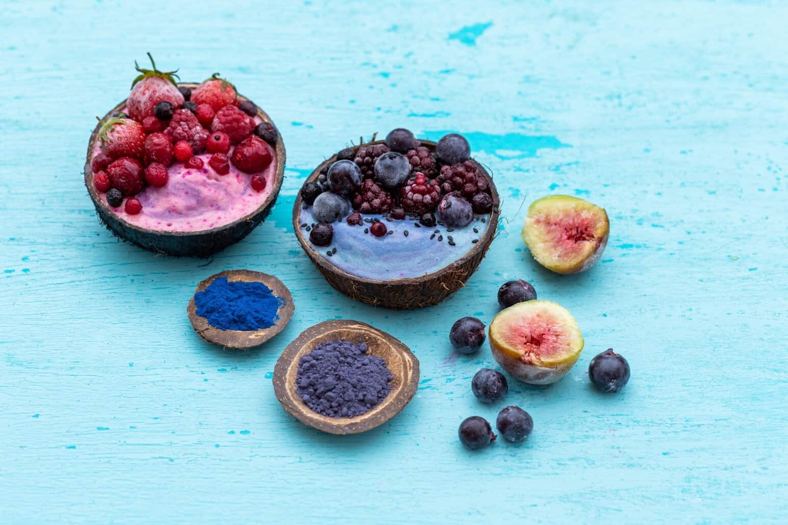 NutriFusion fruit powders beside bowls with berries and fresh figs on a blue surface. 