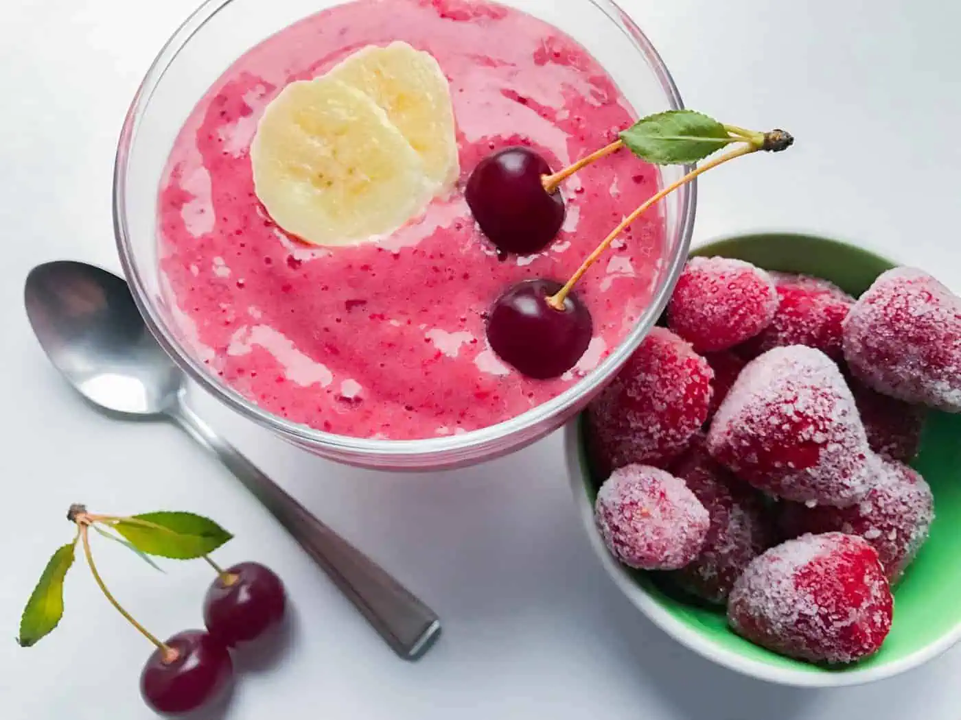 NutriFusion-inspired smoothie topped with banana slices and cherries beside a bowl of frozen berries.