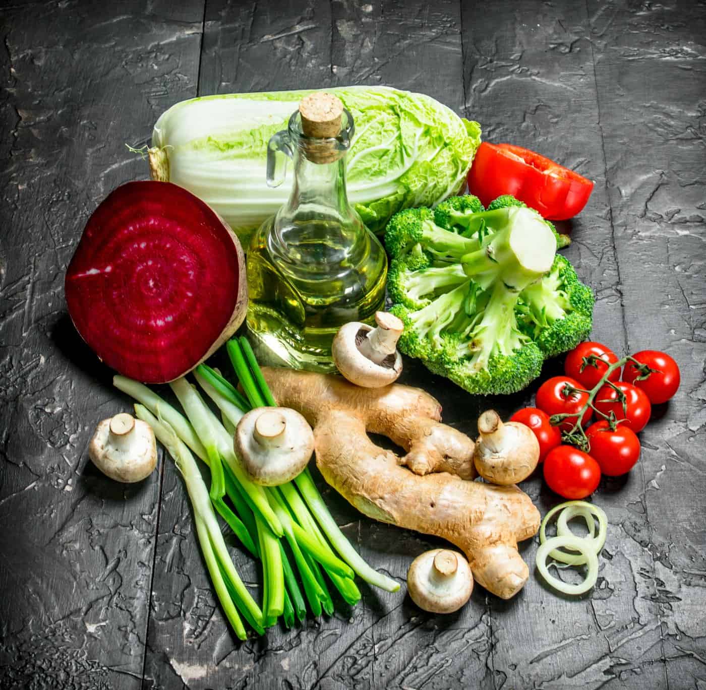 Whole vegetables, including beetroot, broccoli, mushrooms, ginger, tomatoes, and leafy greens, arranged on a dark surface.