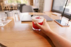 Hand holding a cranberry drink with foam on top on a wooden table.