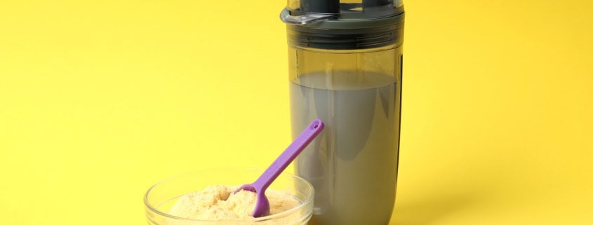 Protein powder in a glass bowl with a scoop beside a shaker bottle for NutriFusion blend.