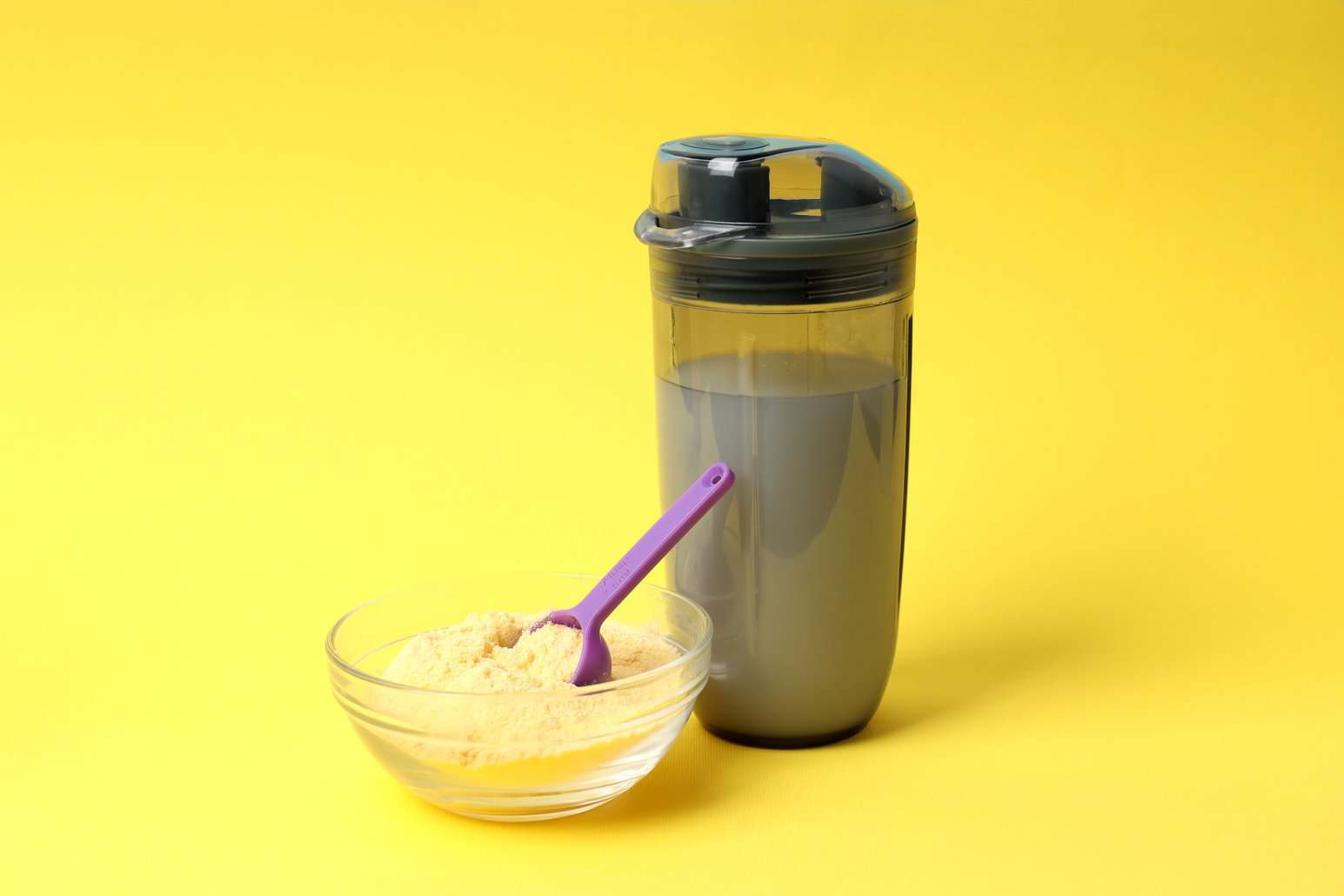 Protein powder in a glass bowl with a scoop beside a shaker bottle for NutriFusion blend.