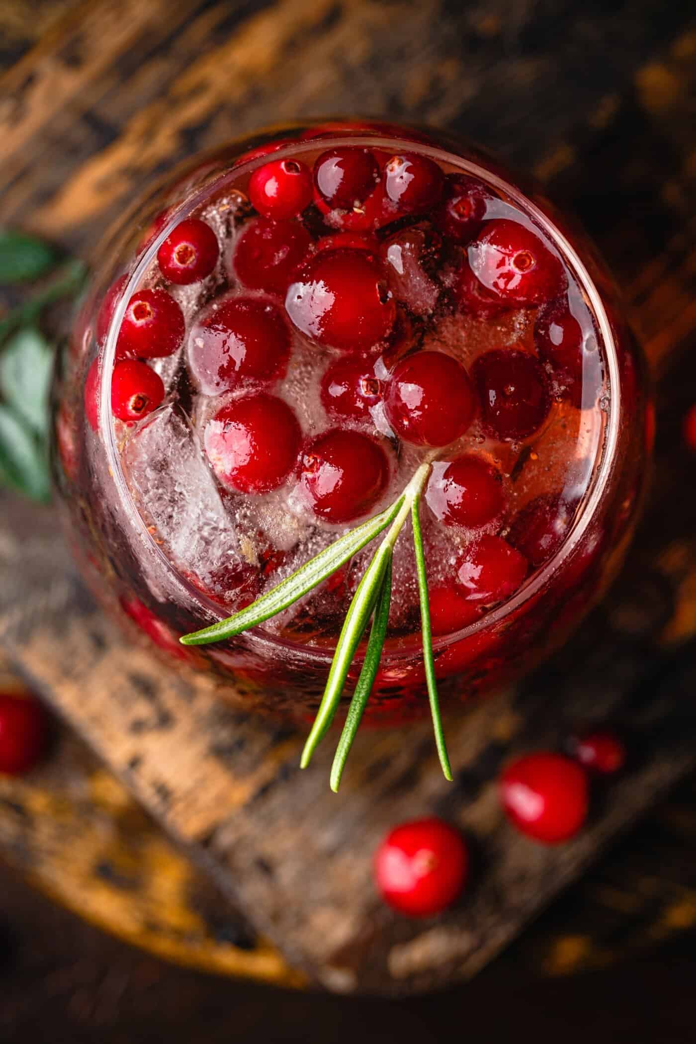 Glass of sparkling cranberry drink infused with NutriFusion blend, topped with ice, and rosemary garnish.