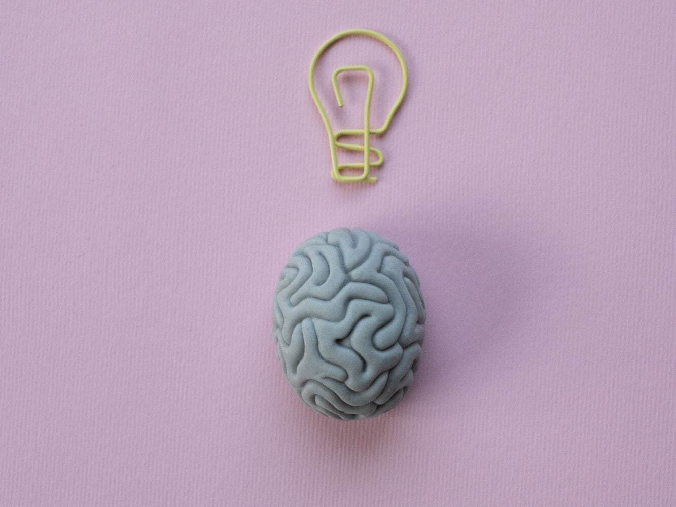 This photo shows a gray brain with light bulb symbol on a pastel background