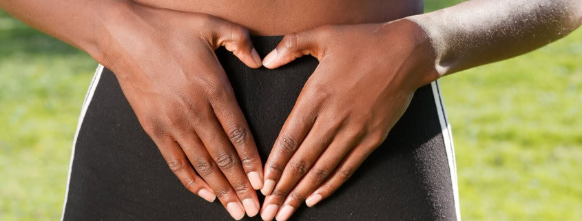 This photo features a person forming a heart with her hands over her gut